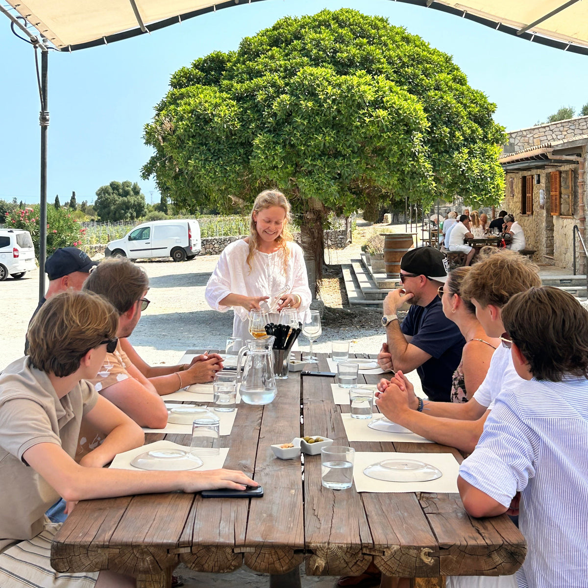 Guests enjoying a guided wine tasting with a host at an outdoor table at Bodegas Can Vidalet in Mallorca.