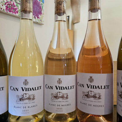Tres botellas de vino de Bodegas Can Vidalet (Blanc de Blancs, Blanc de Negres y otro vino rosado) alineadas sobre una mesa, con sus etiquetas claramente visibles.